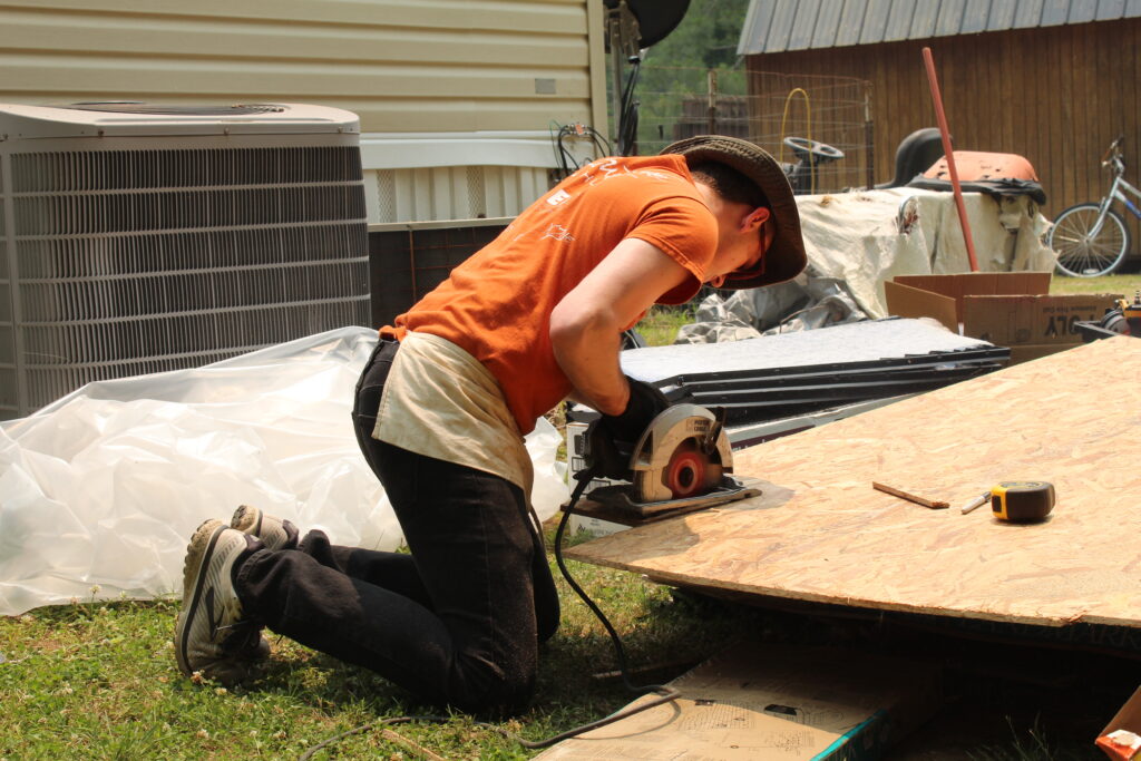 Young man wearing a hat using a circular saw to cut wood