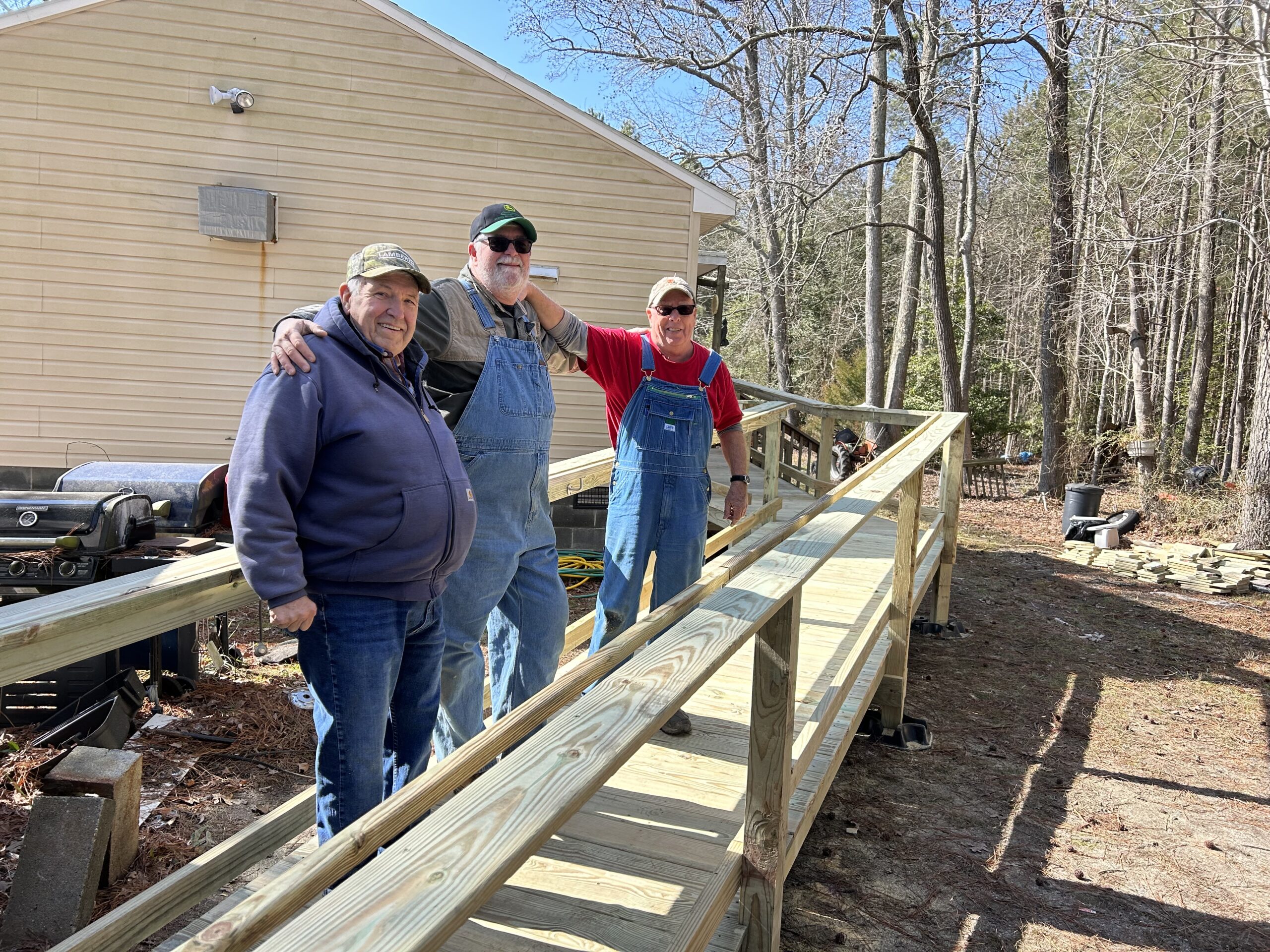 Group of three male volunteers standing on a newly constructed wheelchair ramp near Ocran, Virginia on a sunny day in winter.