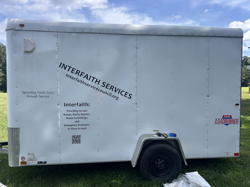 A utility trailer that has been outfitted to serve as the official work trailer for Interfaith Service Council. It has the name, and contact information included on the side of the trailer.