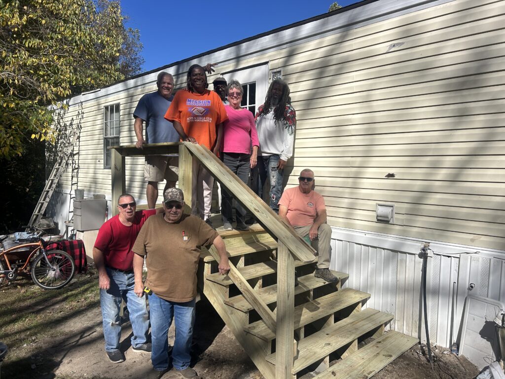 Group of volunteers standing with a homeowner on their newly built steps on the outside of their house in Lancaster, Virginia.