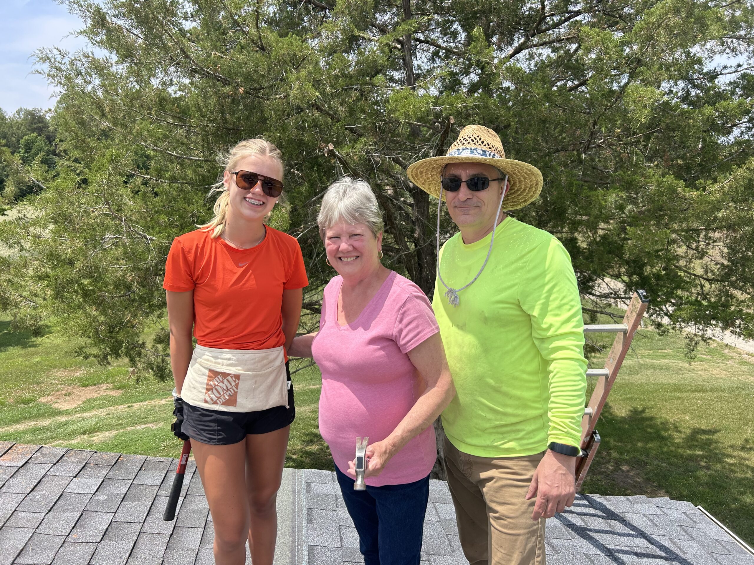 Three volunteers, a young girl, an older lady, and a older man take a break to pose for a picture during the June 2026 mission trip to build a ramp and fix a roof.